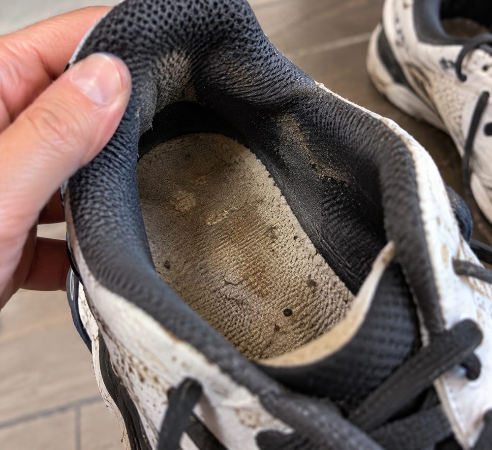 The inside of a worn sneaker held open, showing a dark grimy insole